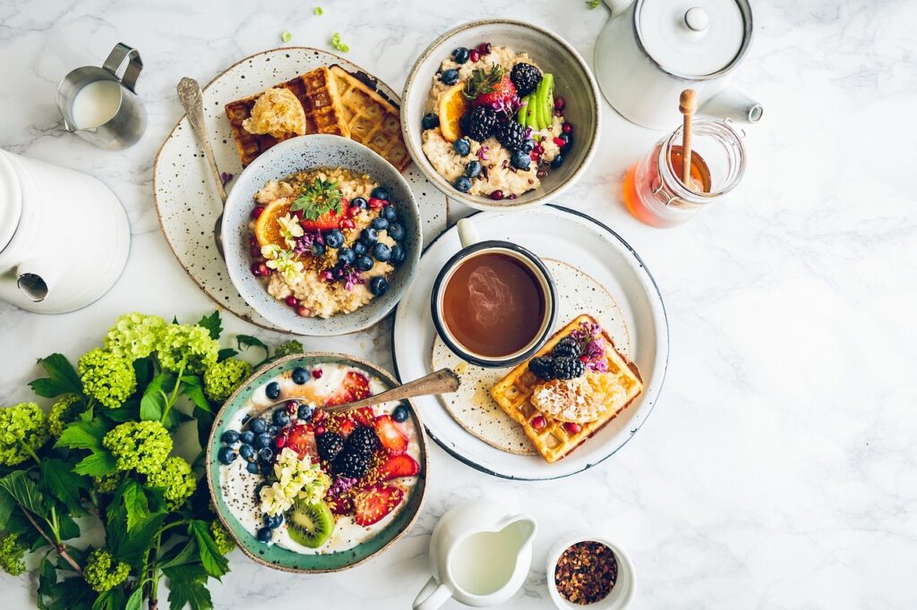 A beautifully arranged breakfast spread featuring oatmeal bowls with fresh fruits, waffles with honey, a cup of coffee, and a jar of honey on a marble countertop.