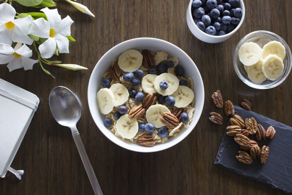 A healthy breakfast bowl with chia seeds, banana slices, blackberries, strawberries, and kiwi, served with a glass of orange juice, avocado, whole grain toast, and fresh fruits on a rustic wooden table.