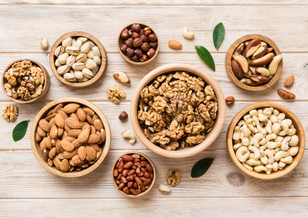 A variety of healthy nuts and seeds, including walnuts, almonds, cashews, and pistachios, displayed in wooden bowls on a rustic wooden surface.